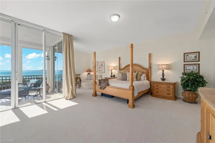Bedroom featuring a water view, access to outside, a wall of windows, and light carpet