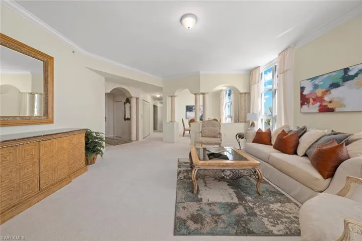 Carpeted living area with arched walkways, ornamental molding, and ornate columns