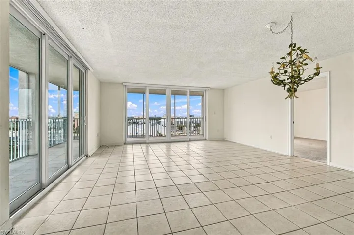 Expansive room with large format tile flooring, multiple sliding glass doors, and a decorative chandelier