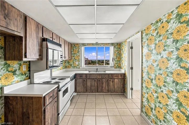 Integrated appliances, wood-finish cabinetry, light-toned countertops, tiled flooring, and a window with expansive views
