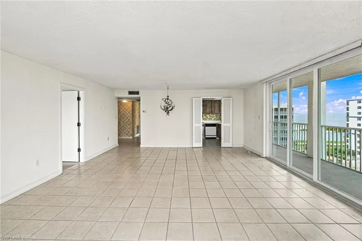Spacious open-concept living area featuring neutral tile flooring throughout, abundant natural light from expansive sliding glass doors and windows, and multiple room access points