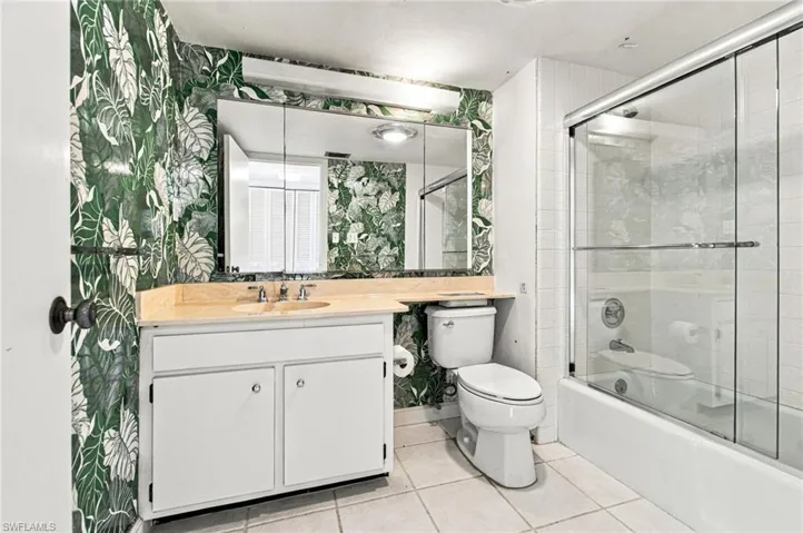 Vanity with a light-toned countertop, a mirrored medicine cabinet, a built-in sink, and a shower-tub combination with a sliding glass door