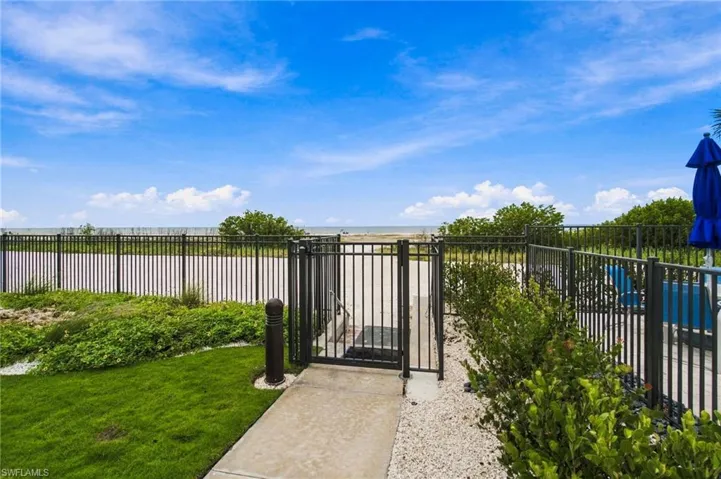 Gated access to shoreline, concrete pathway, manicured lawn, gravel landscaping, and established shrubbery