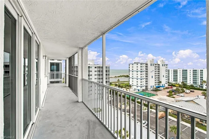 Expansive balcony with concrete flooring, white stucco walls, and a metal railing system