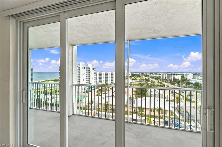 Sliding glass doors opening to a private balcony with metal railings and a distant ocean horizon
