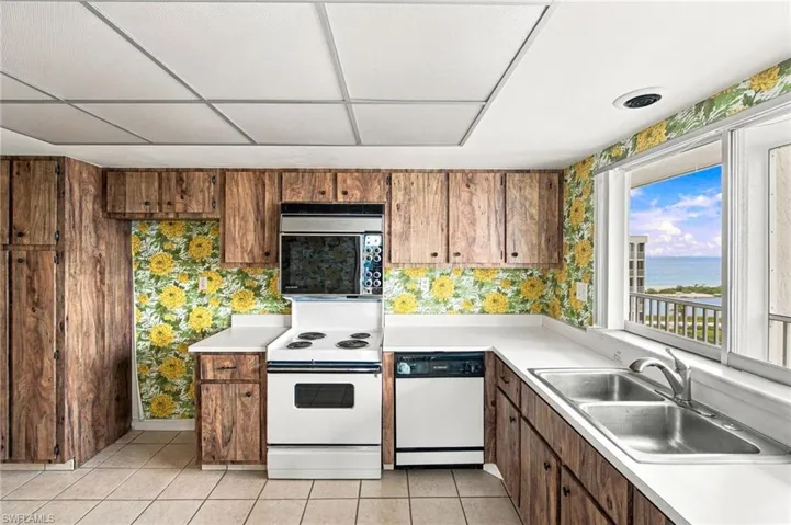 Galley kitchen featuring wood-finish cabinetry, white countertops, a stainless steel double basin sink, and a window with water scenery