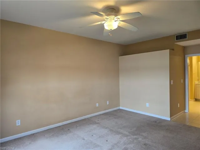 Large master bedroom with light colored carpet and a ceiling fan