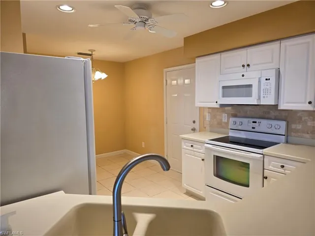 Kitchen featuring white cabinets, white appliances, light countertops, a ceiling fan, and decorative backsplash