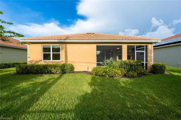 Rear view of property featuring a yard, a tile roof, stucco siding, and a sunroom