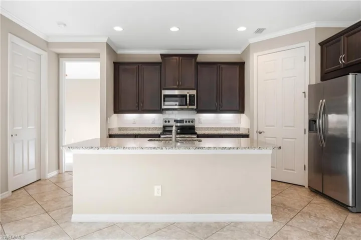 Kitchen with backsplash, stainless steel appliances, crown molding, dark brown cabinetry, and light tile patterned flooring