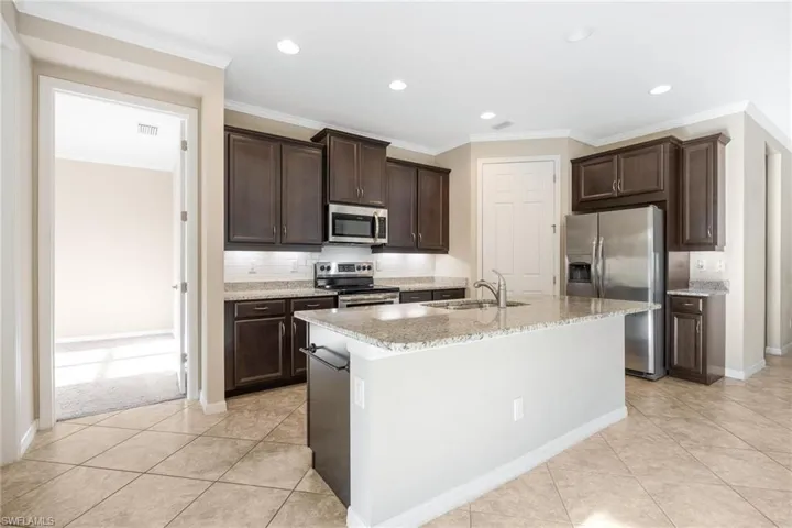 Kitchen with decorative backsplash, stainless steel appliances, dark brown cabinets, ornamental molding, and an island with sink