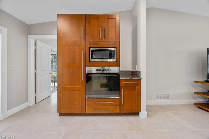 Kitchen with appliances with stainless steel finishes, brown cabinets, dark stone countertops, light tile patterned floors, and lofted ceiling