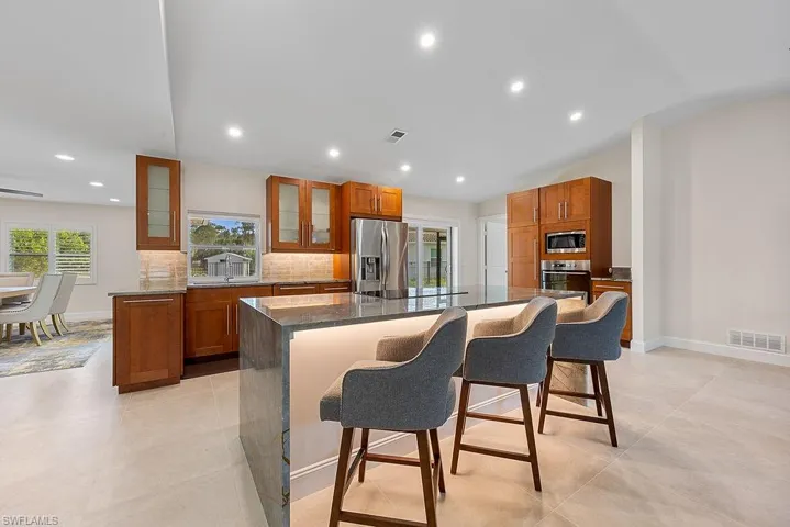 Kitchen with glass insert cabinets, a kitchen breakfast bar, dark stone countertops, brown cabinetry, and backsplash
