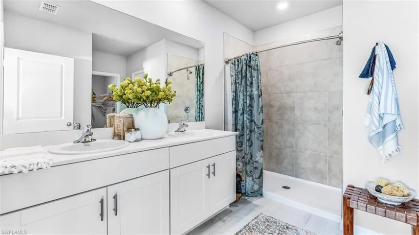 Model home. Bathroom with double vanity, a shower stall, and a spacious closet
