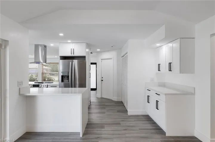 View of Kitchen from family room with white cabinets, vaulted ceiling, stainless steel appliances, light hardwood / wood-style vinyl floors, and coffee/ bar area.