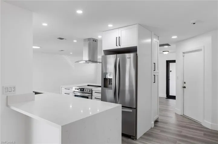Kitchen with white cabinets, light wood-type flooring, appliances with stainless steel finishes, kitchen peninsula, and island exhaust hood