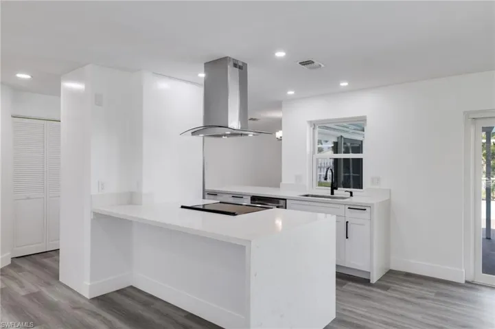 Kitchen with light hardwood / wood-style vinyl flooring, white cabinetry, sink, kitchen peninsula, and island range hood