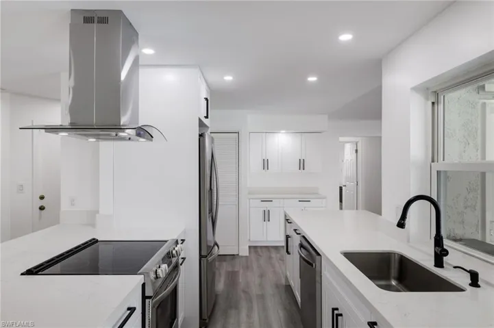 Kitchen with stainless steel appliances, light stone counters, sink, island exhaust hood, and white cabinets