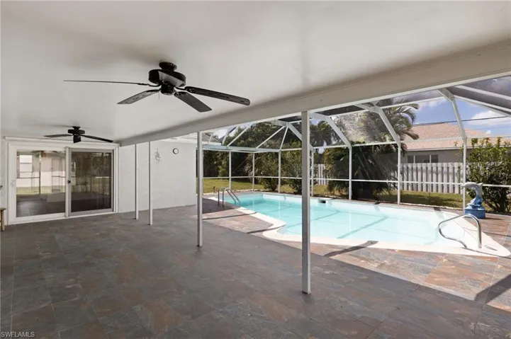 View of pool with screen enclosure, a patio area, and ceiling fans.