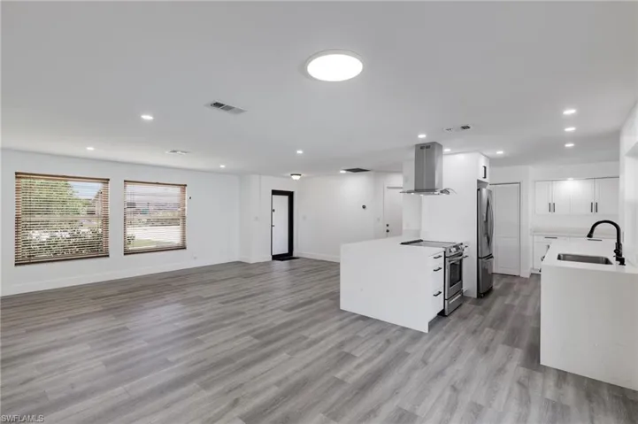 View from Dining area of Kitchen with exhaust hood, light hardwood / wood-style vinyl flooring, appliances with stainless steel finishes, sink, and white cabinetry
