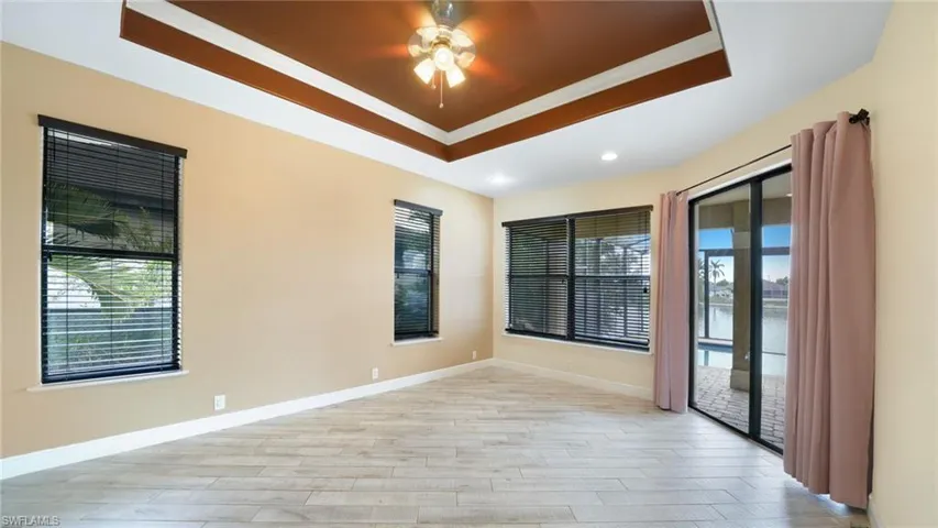Primary bedroom with soaring tray ceiling, double slider AND double windows looking out on the pool & lake, and windows too to let in the beautiful Florida sunshine.