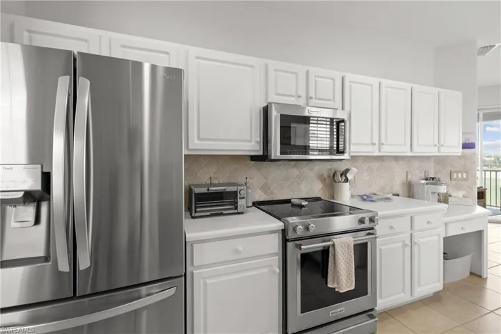Kitchen featuring stainless steel appliances, decorative backsplash, light tile patterned floors, and white cabinets