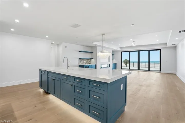 Kitchen with blue cabinetry, a center island with sink, open floor plan, light wood-style floors, and a tray ceiling
