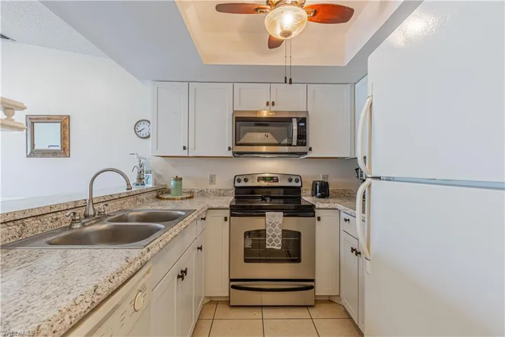 Kitchen with appliances with stainless steel finishes, white cabinets, light tile patterned floors, a raised ceiling, and a ceiling fan