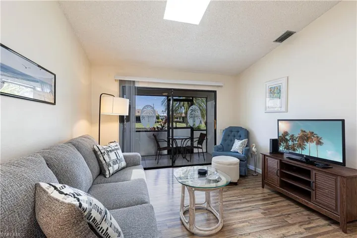 Living room with a textured ceiling, wood finished floors, and lofted ceiling