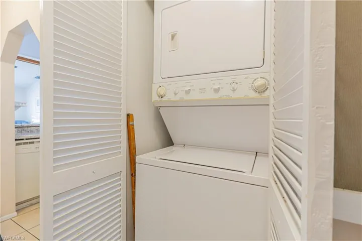 Laundry area with stacked washing machine and dryer and light tile patterned flooring