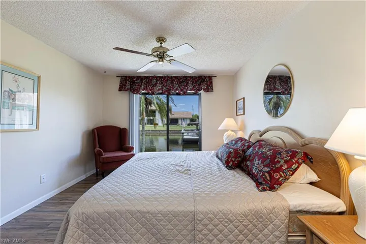Bedroom featuring a textured ceiling, wood finished floors, a water view, ceiling fan, and access to outside