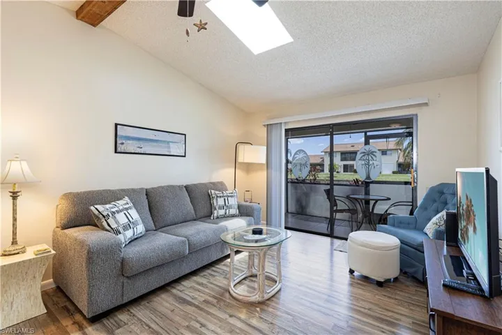 Living area featuring lofted ceiling, a textured ceiling, wood finished floors, a skylight, and ceiling fan