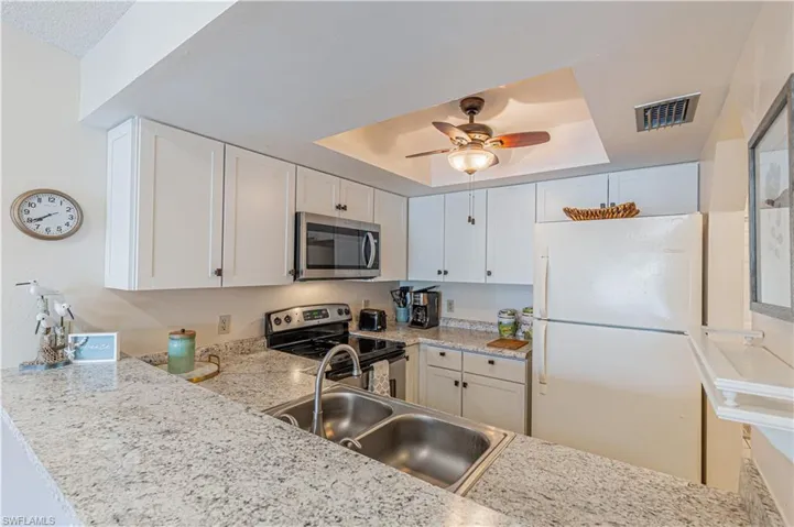 Kitchen featuring white cabinetry, appliances with stainless steel finishes, a raised ceiling, ceiling fan, and light stone countertops