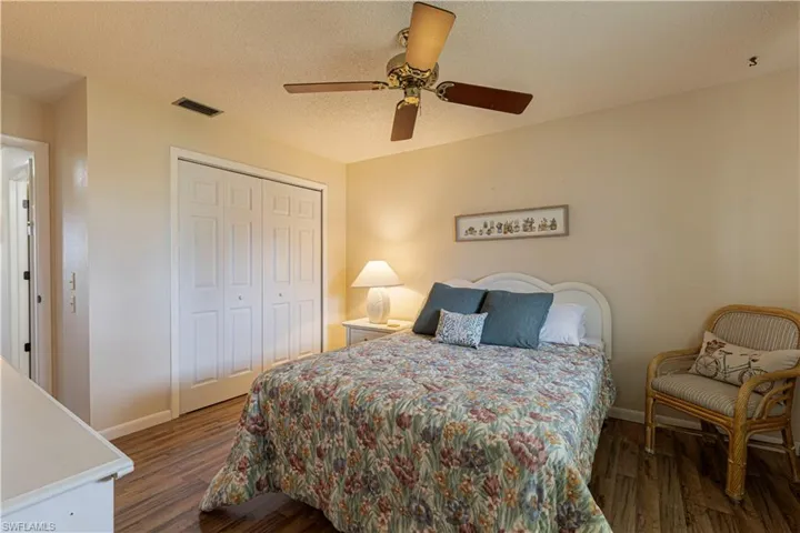 Bedroom with a textured ceiling, dark wood-style floors, a closet, and a ceiling fan
