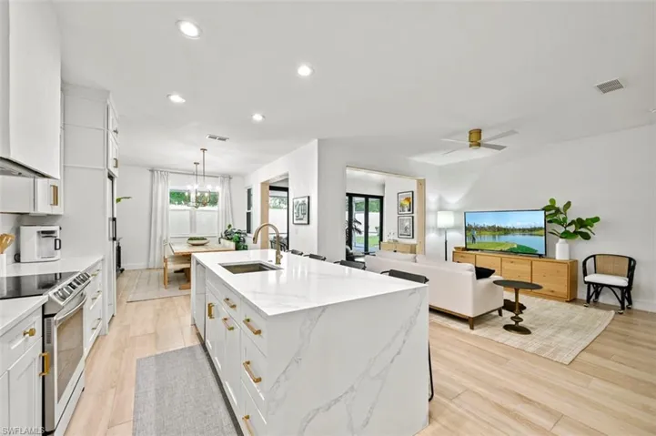 Kitchen with a sink, stainless steel electric range oven, a kitchen island with sink, white cabinets, and recessed lighting