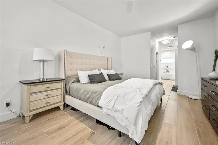 Bedroom with light wood-style flooring, ensuite bath, baseboards, and ceiling fan