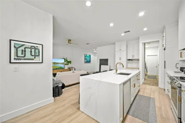 Kitchen featuring a sink, stainless steel range, white cabinetry, a center island with sink, and ceiling fan