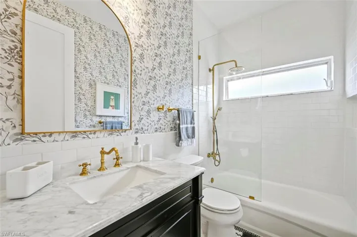 Full bathroom with wallpapered walls, vanity, toilet, shower / bath combination, and tile walls