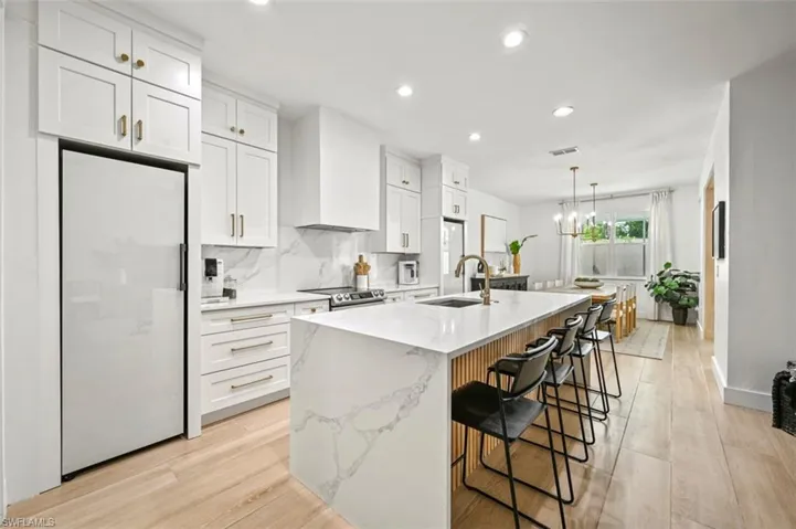 Kitchen with freestanding refrigerator, wall chimney range hood, stainless steel electric range, a kitchen island with sink, and a sink
