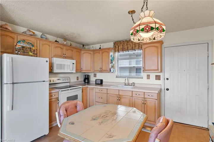 Kitchen with a textured ceiling, white appliances, sink, and decorative light fixtures