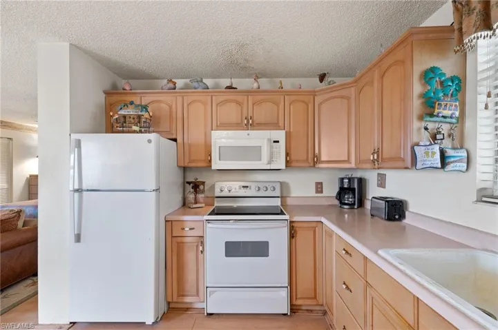 Kitchen featuring sink, light brown cabinetry, a textured ceiling, and white appliances