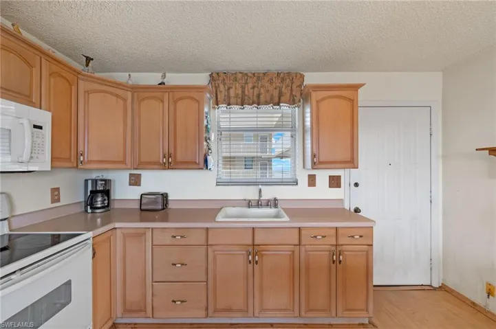 Kitchen featuring sink, light wood-type flooring, a textured ceiling, and white appliances