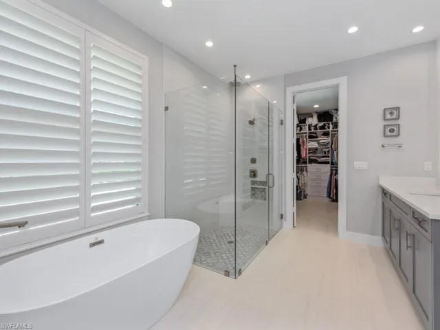 Bathroom featuring a spacious closet, a stall shower, vanity, a freestanding bath, and recessed lighting