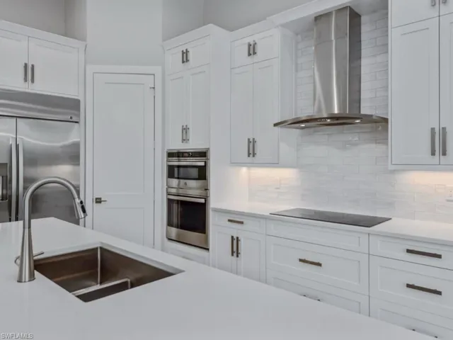 Kitchen with wall chimney range hood, stainless steel appliances, white cabinetry, decorative backsplash, and light stone countertops