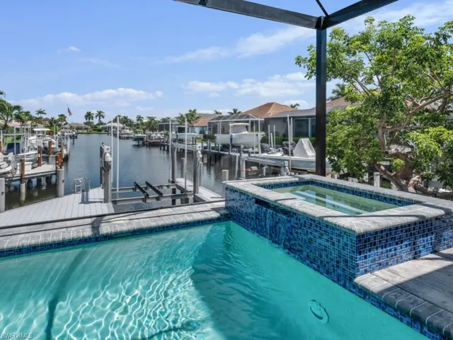 View of swimming pool with boat lift, a water view, a boat dock, and a pool with connected hot tub