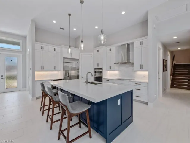 Kitchen with decorative backsplash, white cabinetry, wall chimney exhaust hood, a spacious island, and decorative light fixtures