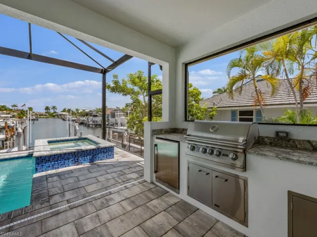 View of patio featuring a water view, a sunroom, an outdoor kitchen, a pool with connected hot tub, and a lanai