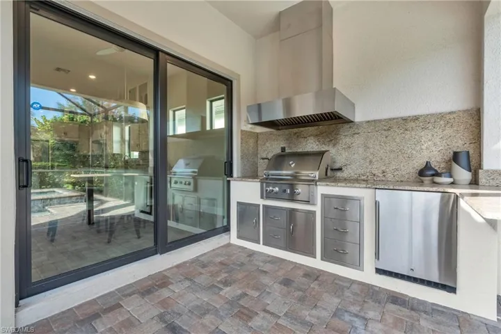 Kitchen with wall chimney exhaust hood, stainless steel fridge, light stone counters, and backsplash