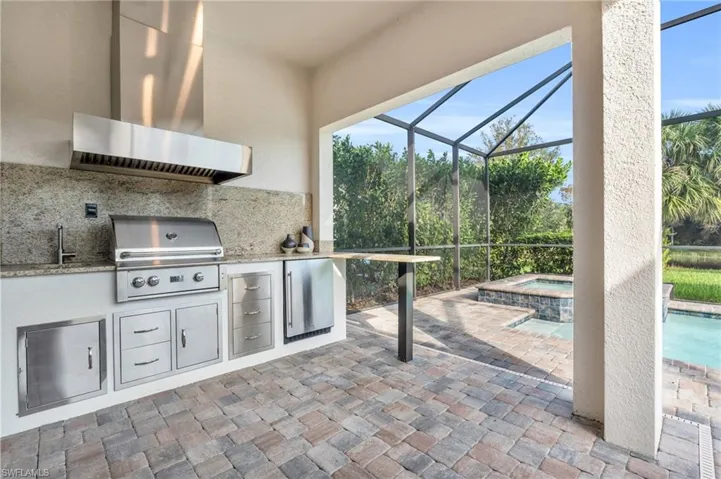 View of patio featuring a grill, exterior kitchen, a pool with hot tub, sink, and a lanai