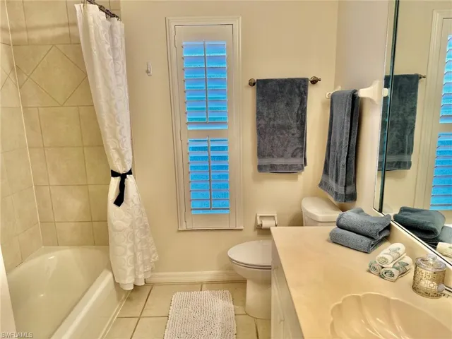 Full bathroom with tile patterned flooring, vanity, toilet, shower / bathtub combination with curtain, and baseboards